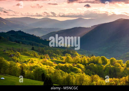 Splendida campagna montuosa al tramonto. bellissimo paesaggio con viola cielo sopra le boscose colline illuminate dai raggi del sole. Foto Stock