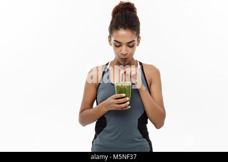 Sana e concetto di Fitness - bella americana africana di lady in abbigliamento fitness bere sano bevanda vegetale. Isolato su sfondo bianco. Foto Stock