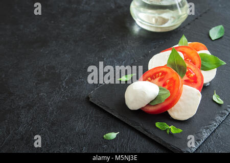 Tradizionale Italiano insalata caprese - fette di pomodoro, mozzarella e basilico in pietra scura sullo sfondo, vista dall'alto, copyspace. Insalata caprese, italiano Foto Stock