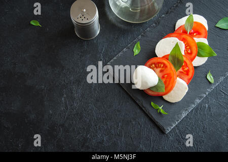 Tradizionale Italiano insalata caprese - fette di pomodoro, mozzarella e basilico in pietra scura sullo sfondo, vista dall'alto, copyspace. Insalata caprese, italiano Foto Stock