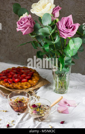 Tavolo da pranzo con fiori, tè alle erbe e torta alle fragole, stile rustico Foto Stock