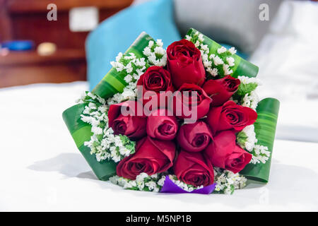 Un mazzo di rose rosse giacente su un letto. Foto Stock