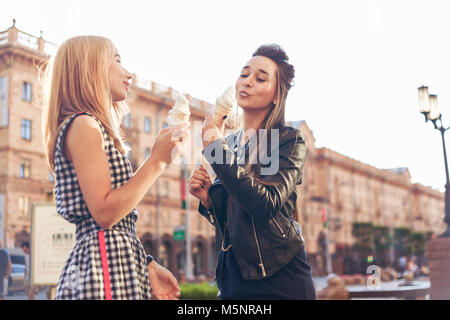 Due migliori amici avente gelato insieme all'esterno. Le giovani donne a mangiare il gelato e ridere. Foto Stock