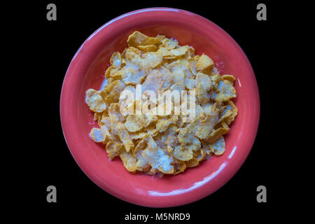 Una ciotola di cornflake in un piatto rosso isolata contro uno sfondo nero. Foto Stock
