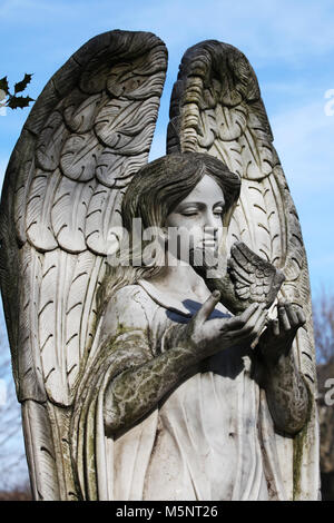 Una lapide che mostra la figura di un angelo tenendo una colomba siede contro il cielo in un cimitero di Edimburgo Foto Stock