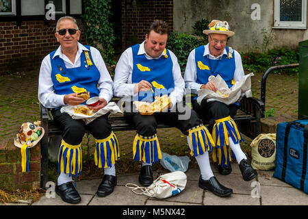 Un gruppo di uomini di Morris a sedersi su una parete di mangiare pesce e patatine durante l annuale Lewes Folk Festival, Lewes, Sussex, Regno Unito Foto Stock