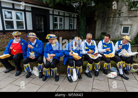 Un gruppo di uomini di Morris a sedersi su una parete di mangiare pesce e patatine durante l annuale Lewes Folk Festival, Lewes, Sussex, Regno Unito Foto Stock