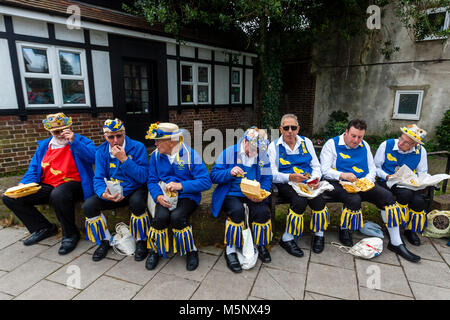 Un gruppo di uomini di Morris a sedersi su una parete di mangiare pesce e patatine durante l annuale Lewes Folk Festival, Lewes, Sussex, Regno Unito Foto Stock