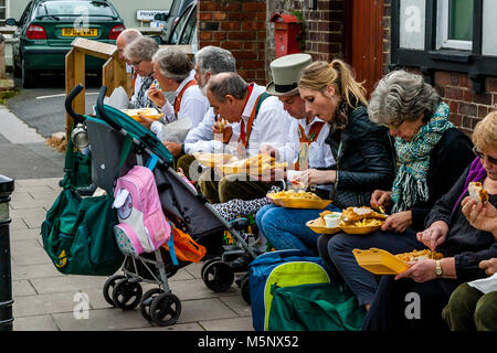 Un gruppo di ballerini di Morris a sedersi su una parete di mangiare pesce e patatine durante l annuale Lewes Folk Festival, Lewes, Sussex, Regno Unito Foto Stock