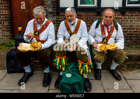 Un gruppo di uomini di Morris a sedersi su una parete di mangiare pesce e patatine durante l annuale Lewes Folk Festival, Lewes, Sussex, Regno Unito Foto Stock