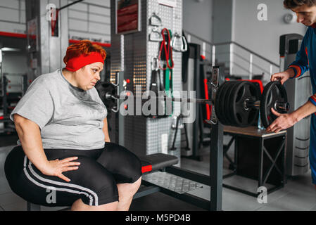 Il sovrappeso sudati donna su allenamento con barbell in palestra. Calorie bruciare, femmina obesi in persona lo sport club Foto Stock