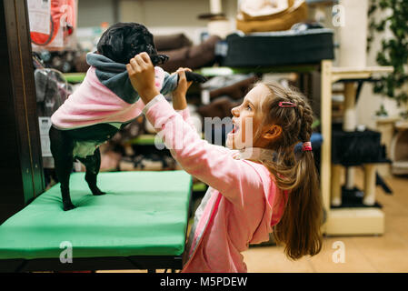 Bambina provare su vestiti per puppy in pet shop. Kid clienti che acquistano cani complessivamente in petshop, prodotti per animali domestici Foto Stock