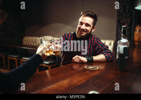 Due uomini clink bicchieri in un bar, amici bere alcool e divertirsi. Felice svago in pub Foto Stock