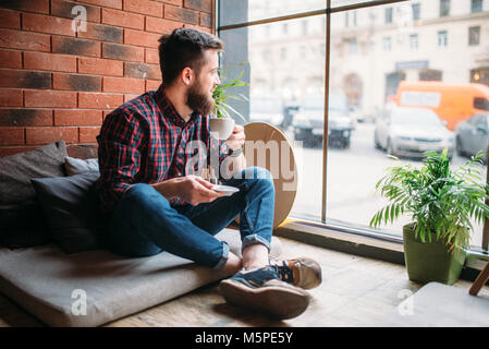 Un maschio visitatore seduto in casa del caffè nelle bevande bevanda. Persona di sesso maschile tempo libero in pub Foto Stock
