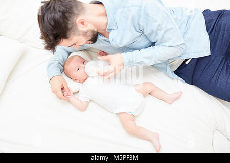 Il marito come un padre amoroso alimenta il bambino con il latte dalla bottiglia Foto Stock