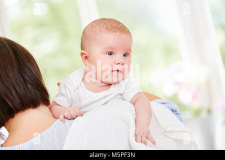 Piccolo bambino sulle braccia della madre guarda curiosamente nel mondo Foto Stock