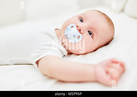 Neonato giace sulla schiena con un ciuccio in bocca Foto Stock