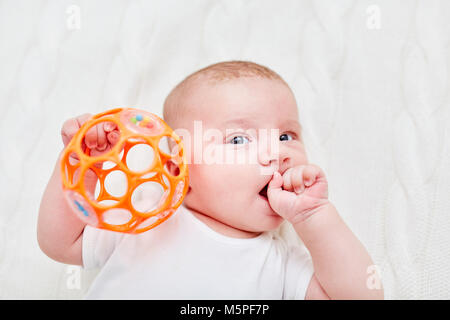 Carino baby tenendo il sonaglio saldamente in una mano e la suzione del pollice Foto Stock