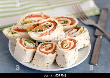 Rotoli di sottili frittelle con salmone affumicato e crema di formaggio, erba cipollina e lattuga. Foto Stock