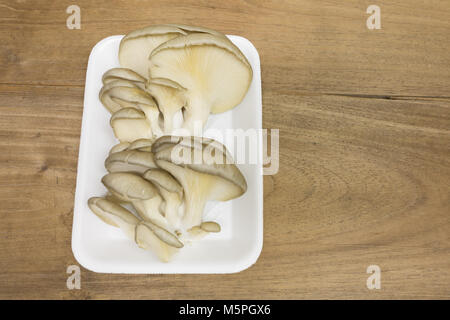 Oyster (fungo Pleurotus ostreatus) in bianco styrofoam vassoio per alimenti, centro a sinistra, su sfondo di legno Foto Stock