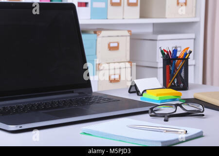 Close-up di comodo posto di lavoro in un ufficio con computer portatile, un mouse, notebook, bicchieri, penna e altre apparecchiature posa sulla tavola su mobili di sfocatura dello sfondo. Foto Stock