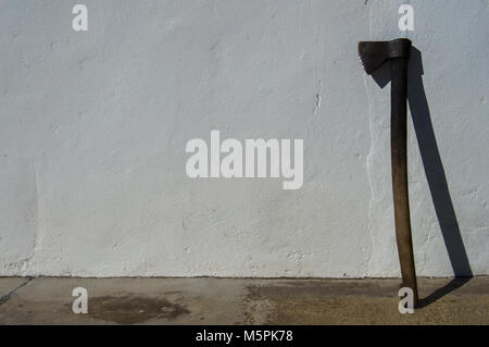 Vecchio e sporco o ax ax in appoggio su una parete bianca. Immagine di un luogo rurale durante una giornata di sole. Lo spazio in bianco per aggiungere elementi. Foto Stock