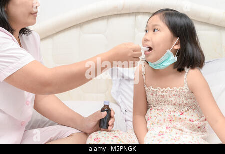 Madre dando la sua figlia sciroppo a causa della influenza e tosse, Health care concept Foto Stock