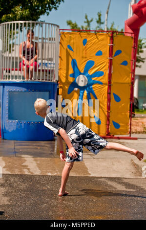 Un ragazzo che colpisce una palla al bersaglio su un dunk serbatoio ad un'estate evento esterno Foto Stock