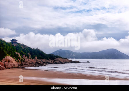 Un edificio cinese e la costa rocciosa a 100 passo beach a bassa marea sull isola di putuoshan Cina su un nuvoloso giorno nella provincia di Zhejiang. Foto Stock