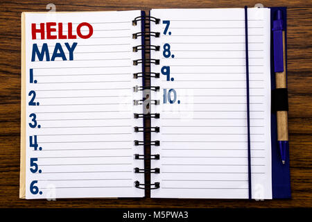 La scrittura di un testo che mostra Ciao maggio mese. Il concetto di business per il prossimo mese di primavera scritta su carta per appunti, sullo sfondo di legno con una penna e un marcatore. Foto Stock