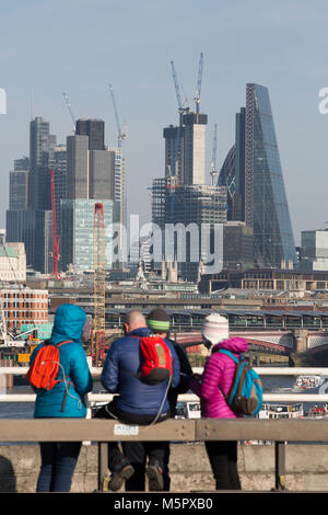 I turisti vestito in abiti invernali in un freddo giorno chiaro, sosta per ammirare la vista dal ponte di Waterloo oltre i grattacieli della City di Londra, Regno Unito Foto Stock