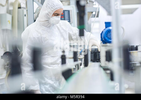 Giovane uomo che indossa tuta e maschera di sicurezza lavorando sulla linea di produzione della moderna fabbrica farmaceutica, ritratto Foto Stock