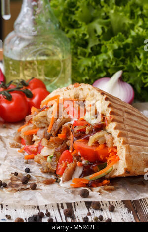 Un piatto di pane pita ripiene di carne alla brace, poi tritate la carne e le verdure fresche. Still-life su uno sfondo di legno. Foto Stock