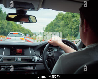 Un interno di auto e autista di una vettura bloccato nel traffico da lavori in corso su un'autostrada. Foto Stock