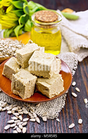 Dolce orientale halva girasole in una piastra, semi di girasole, olio e fiore su tela sullo sfondo di un pannello di legno Foto Stock