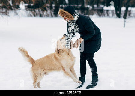 Foto di donna in giacca nera con retriever passeggiate nel parco invernale Foto Stock