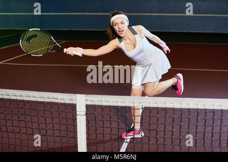 A piena lunghezza ritratto di donna forte giocando a tennis nella corte interna, oscillare racchetta mentre si colpisce la sfera, spazio di copia Foto Stock