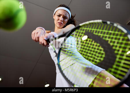 Angolo basso ritratto di donna forte giocando a tennis nella corte interna, concentrarsi sulla racchetta da tennis di colpire la sfera, spazio di copia Foto Stock