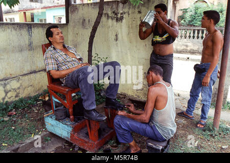 Una pulizia shoeshiner le scarpe di un cliente in Trinidad, Cuba durante il noi emargo era, il cosiddetto periodo speciale Foto Stock