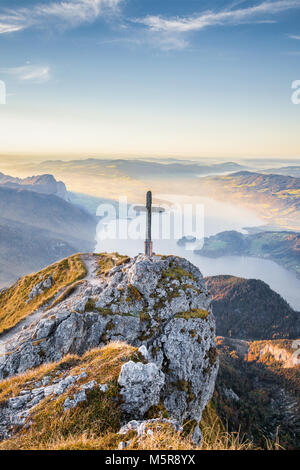 Vista panoramica di un idilliaco paesaggio di montagna delle Alpi con una croce di legno sulla cima di una montagna in golden luce della sera al tramonto. Foto Stock