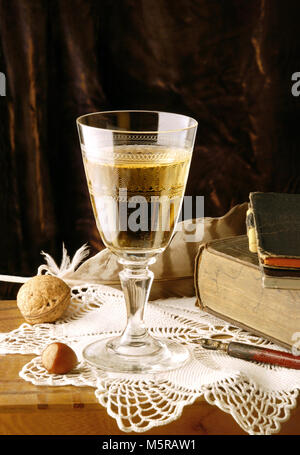 Vintage vita ancora con un bicchiere di vino bianco, dadi, prenota, penna e piuma Foto Stock