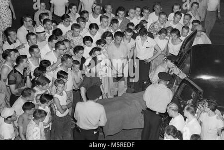 Una folla di vicinato orologi come il corpo della vittima di omicidio viene caricato nel retro della polizia funebre in Chicago, ca. 1955. Foto Stock