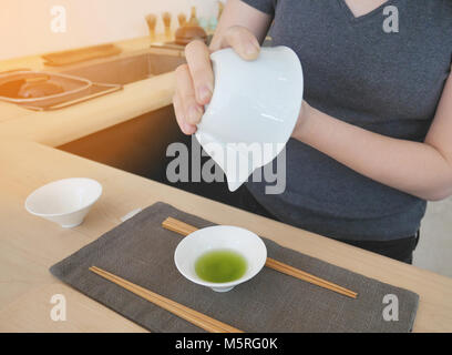 Femmina versando il tè verde al bianco piccola coppa in ceramica su grigio vestire il tappetino in un negozio di tè. Bacchette anche posti pronto per il prossimo di foglie di tè verde eatin Foto Stock