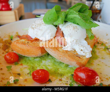 Uova Benedict su toast con bacon, insalata di rucola, avocado e salsa di pomodori Foto Stock
