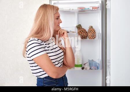 La donna è in piedi di fronte ad un frigo e pensa cosa mangiare Foto Stock