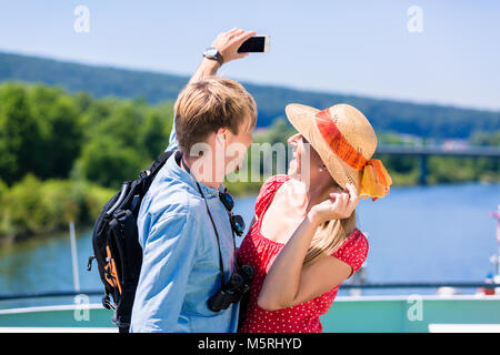 Una giovane coppia in una crociera sul fiume in estate prendendo selfie Foto Stock