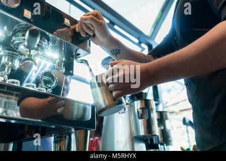 Mano di un barista tenendo una tazza in acciaio inox Foto Stock