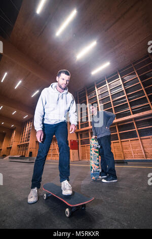Due giovani pattinatori sono la pratica con il loro skateboard in un pattino indoor hall. Foto Stock