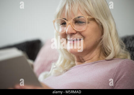 Close up ritratto di felice donna senior in bicchieri libro di lettura Foto Stock