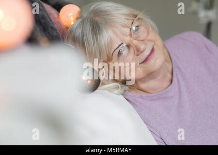 Ritratto di felice senior lady in bicchieri appoggiata su dei cuscini a casa Foto Stock